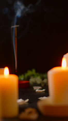 Vertical-Video-Still-Life-Of-Lit-Candles-With-Scattered-Petals-Incense-Stick-Against-Dark-Background-As-Part-Of-Relaxing-Spa-Day-Decor